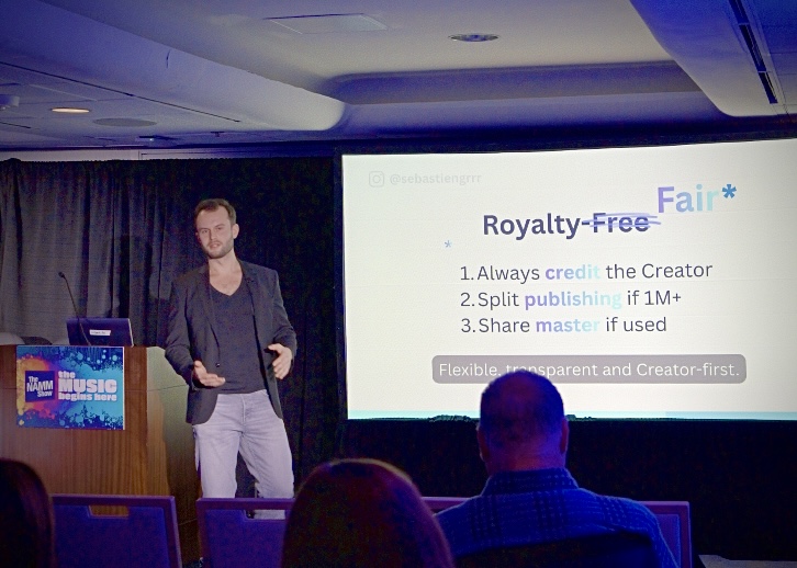 GRAUX sur scène au NAMM Show 2026 à Los Angeles, présentant le modèle Royalty Fair · Royalty-Fair rayé, remplacé par Fair, avec les trois principes Royalty Fair projetés derrière lui